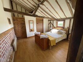 Quarto com teto de madeira, cama com roupa de cama branca, cômoda de madeira e janela.