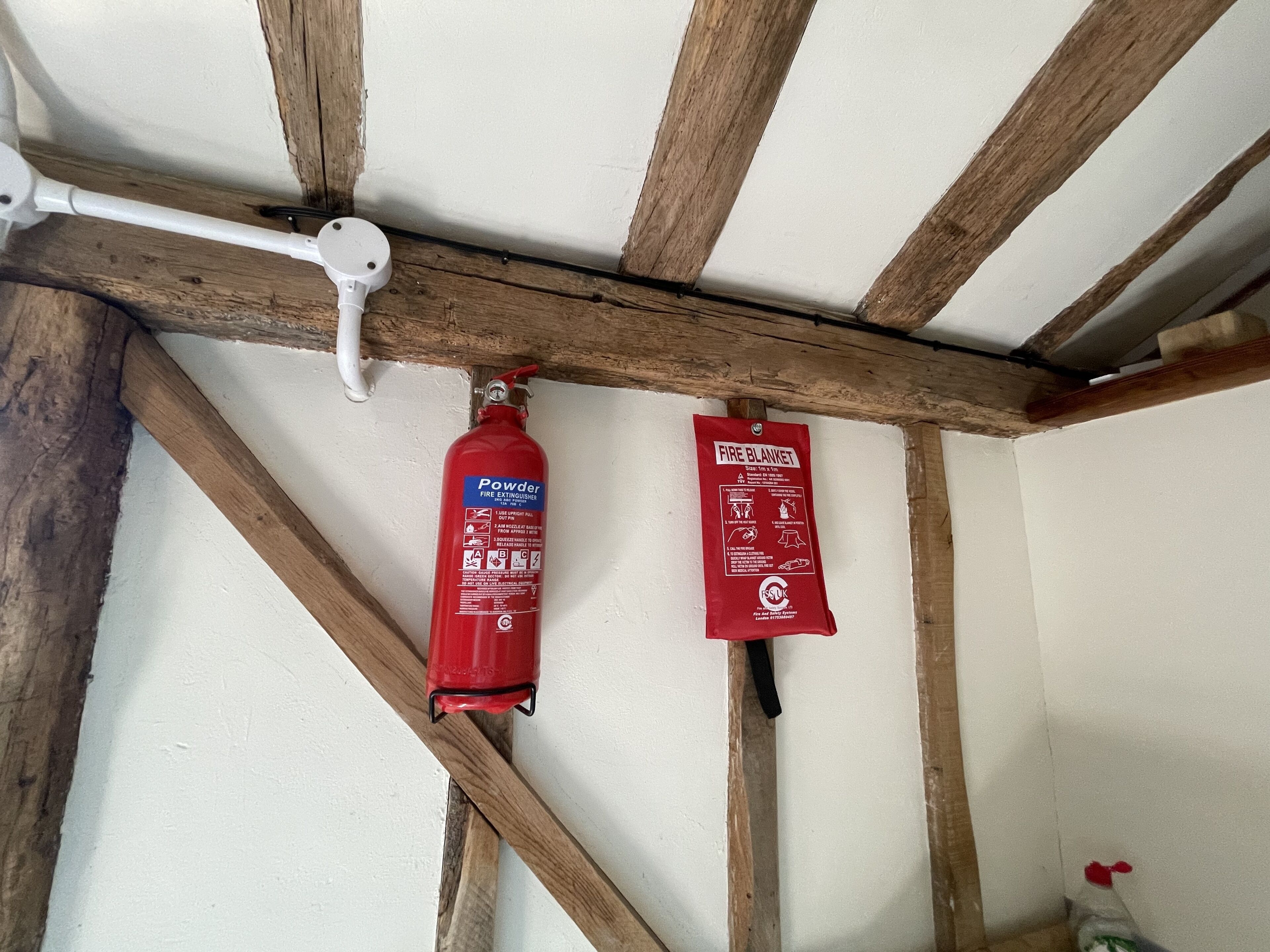 Ein Feuerlöscher und eine Decke zum Löschen von Bränden hängen an einem Holzbalken in einem Raum.