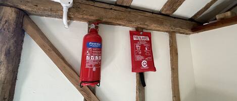 Ein Feuerlöscher und eine Decke zum Löschen von Bränden hängen an einem Holzbalken in einem Raum.