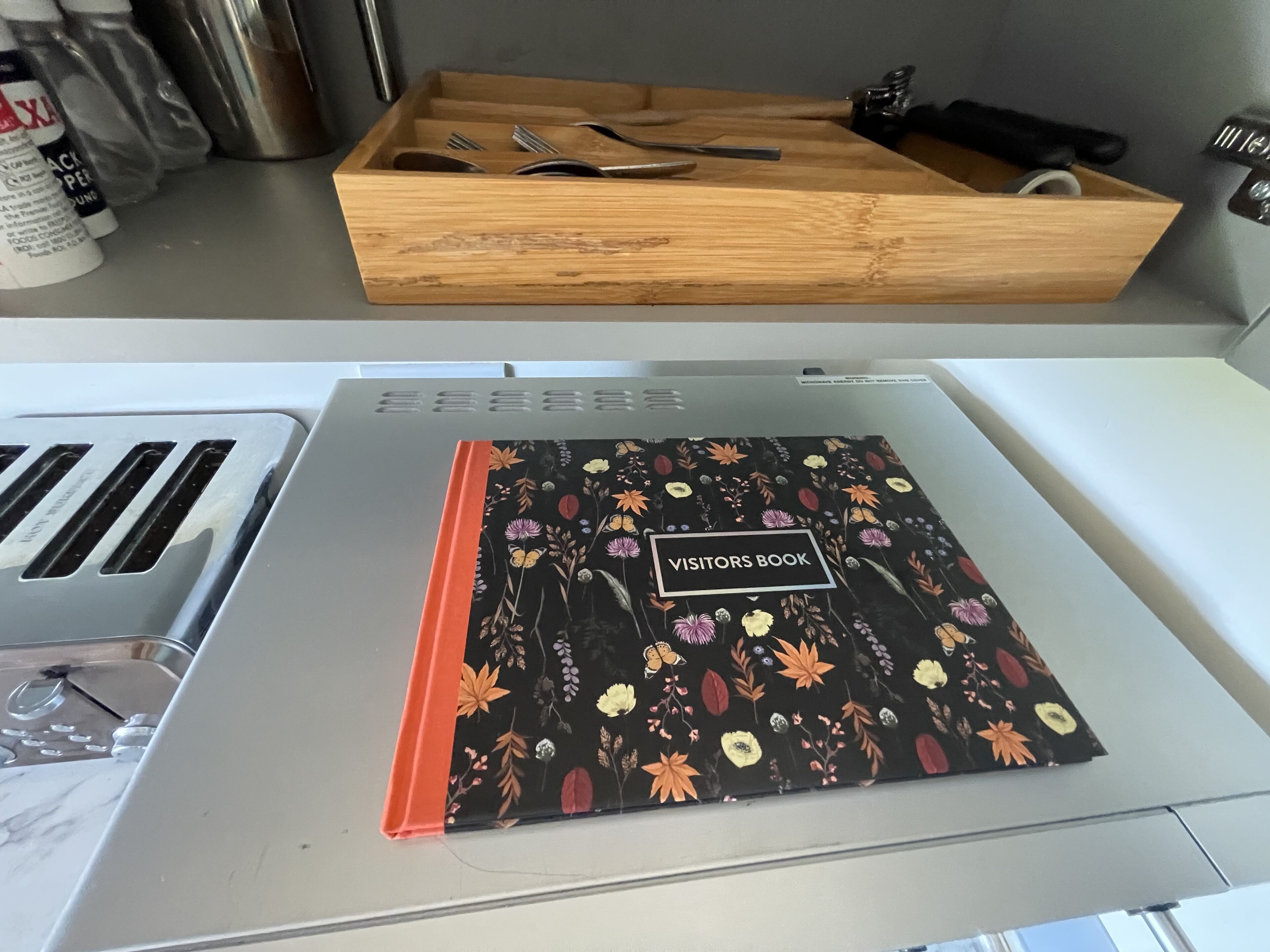 Eine Küchenzeile mit einem Holztisch, der Besteck enthält, einem Gästebuch auf einer Arbeitsfläche und einem Toaster.