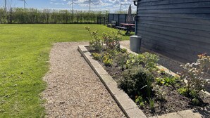 A grassy area with a gravel path, a wooden building, and wind turbines in the background.