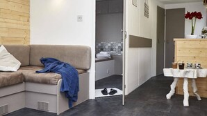 A compact living space with a sofa, a small table with cups, a shower area, and a wooden cabinet. - Cottages, bed and breakfasts in the heart of the North Finistère countryside. (Plouégat-Moysan)