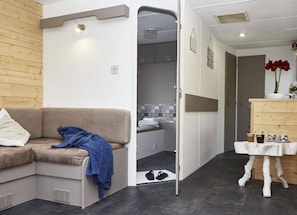 Un espacio habitable compacto con sofá, una mesita con tazas, zona de ducha y un mueble de madera.