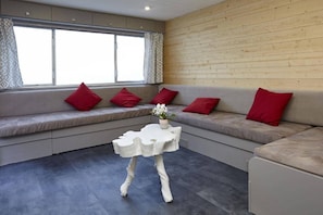 Et moderne interiør med en grå sofa, røde puder, et hvidt bord og et vindue med mønstrede gardiner.