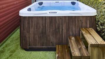 Un bain à remous avec un revêtement extérieur en bois, une terrasse en bois et un bâtiment rouge en arrière-plan.