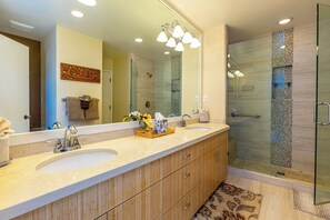 A bathroom with two sinks, a large mirror, and a walk-in shower.
