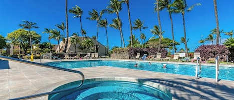 A swimming pool with a hot tub, surrounded by palm trees and lounge chairs.