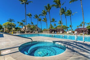 A swimming pool with a hot tub, surrounded by palm trees and lounge chairs.