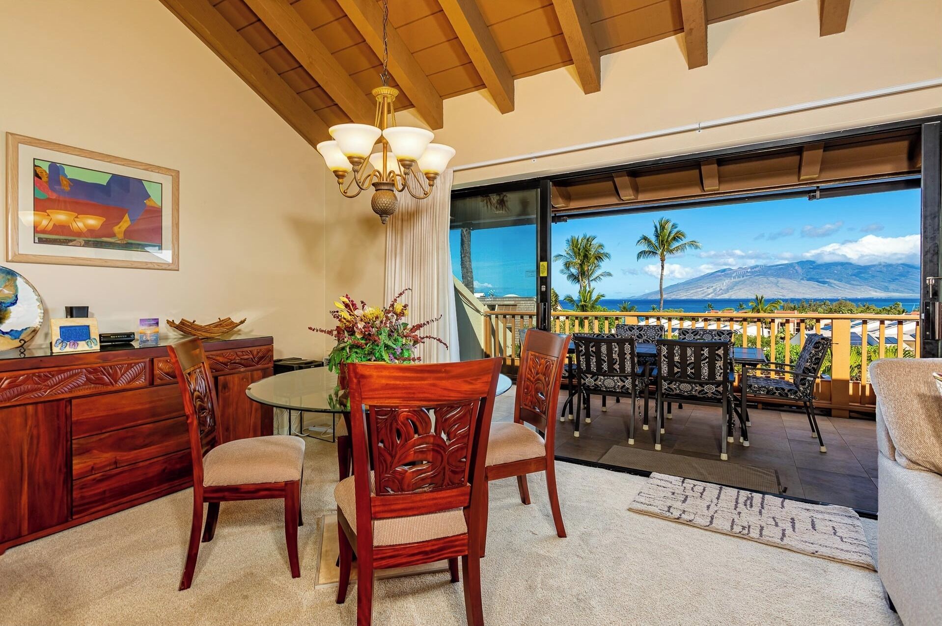 A dining area with a round table and chairs, a chandelier, and a view of the ocean and mountains.