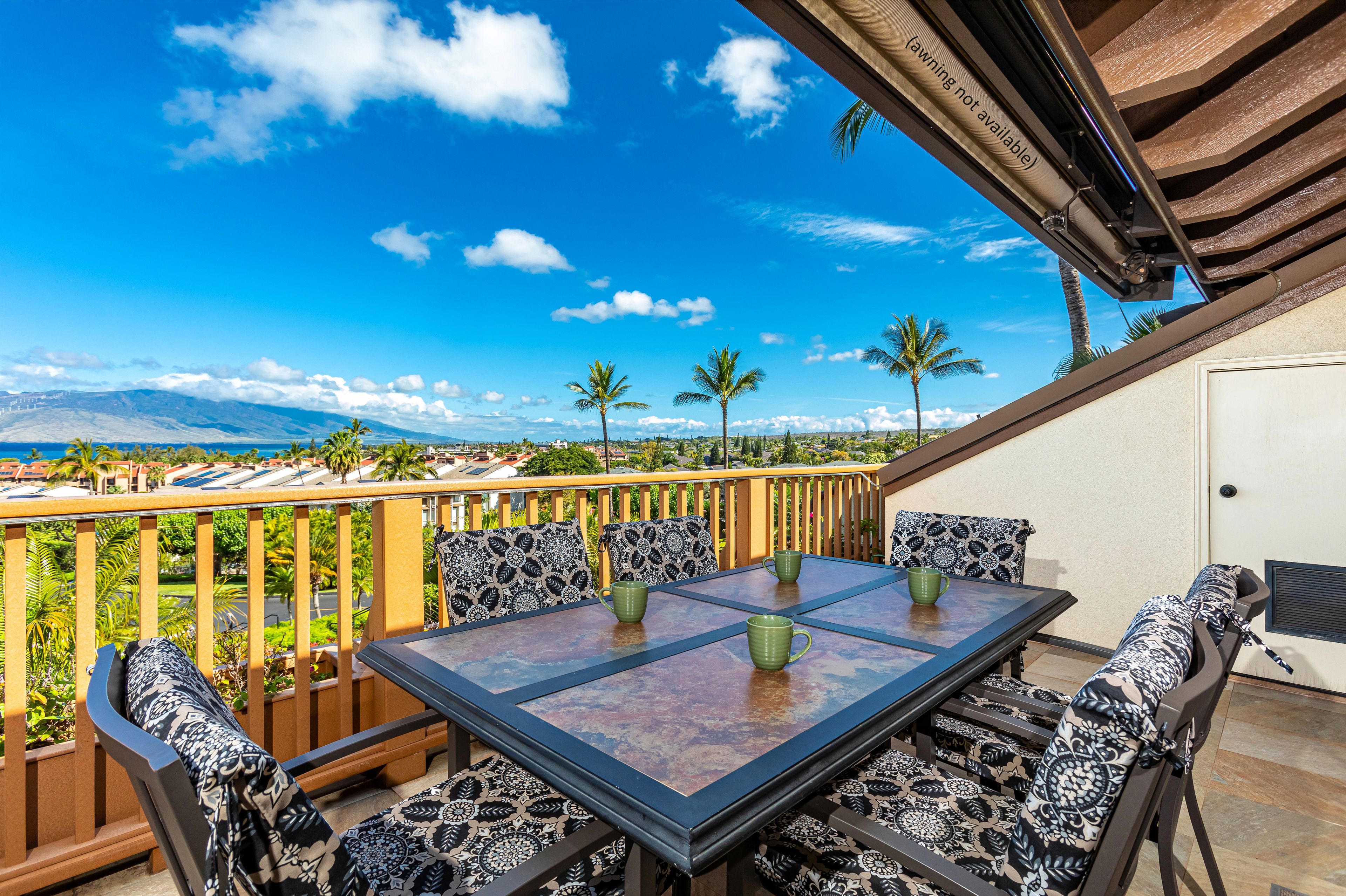 A patio with a table and chairs, a view of palm trees, and a distant mountain range.