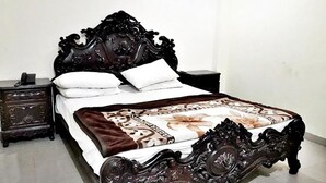 Een bed met een decoratief hoofdeinde en voeteinde, een wit kussen en een bedspreider met bloemenprint.