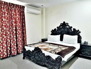 A bedroom with a large bed, a nightstand, a dresser, and a window with curtains.