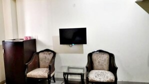 Een kamer met twee fauteuils, een klein tafeltje en een donker houten kastje. Een flatscreen televisie is aan de muur bevestigd.