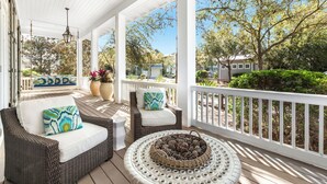 A covered porch with wicker furniture, a white railing, and a view of the surrounding trees and houses. - Chic Cottage 2 Blocks to Dragonfly Pool. With an LSV, Bikes, and More (Santa Rosa Beach)