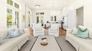 A spacious living room with a fireplace, two white sofas, a coffee table, and a kitchen in the background. - Chic Cottage 2 Blocks to Dragonfly Pool. With an LSV, Bikes, and More (Santa Rosa Beach)