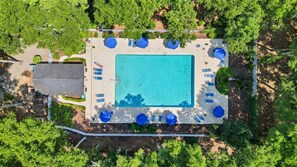 An aerial view of a swimming pool with surrounding lounge chairs and umbrellas, surrounded by trees.