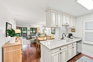 Una cocina moderna con armarios blancos, encimera de mármol y zona de comedor con mesa y sillas.