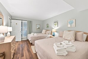 Ein Hotelzimmer mit zwei Betten, Holzboden, einer Tür mit der Beschriftung 'B' und Bildern an den Wänden.