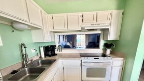 A compact kitchen with white cabinets, a stainless steel sink, a stove, and a coffee maker. - Find your home away from home in the Happy Landing unit (New Smyrna Beach)