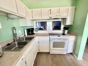 A compact kitchen with white cabinets, a stainless steel sink, a stove, and a coffee maker.