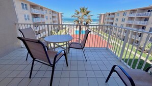 A balcony with a table and chairs, overlooking a swimming pool and a beach. - Find your home away from home in the Happy Landing unit (New Smyrna Beach)