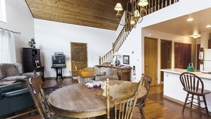Amplia sala de estar con una mesa y sillas de madera, una escalera y una zona de cocina.