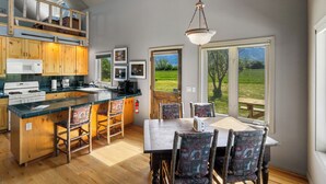 A kitchen with wooden cabinets, a large island, and a dining area with chairs and a table. - Crow Cabin- Cozy Cabin with amazing views on 20 Acres in the Paradise Valley! (Livingston)