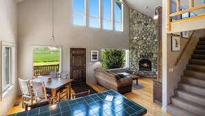 A spacious living area with a stone fireplace, a dining table with chairs, and a staircase leading to an upper level. - Crow Cabin- Cozy Cabin with amazing views on 20 Acres in the Paradise Valley! (Livingston)