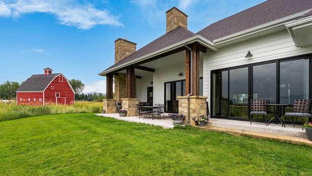 A house with a covered patio, stone chimneys, and a red barn in the background.