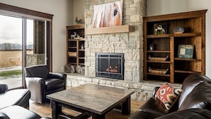 A cozy living room with a stone fireplace, leather furniture, and a view of the outdoors.