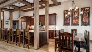 A spacious kitchen with wooden cabinets, a central island, pendant lighting, and a dining area with wooden chairs and a table.