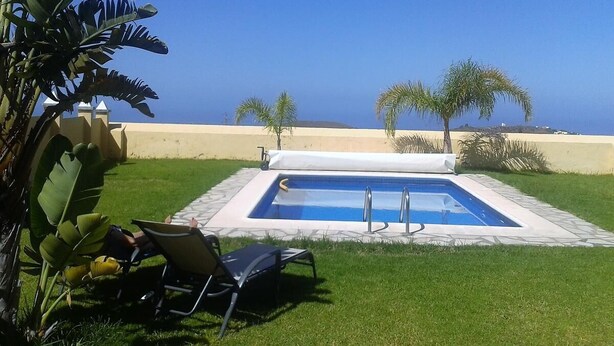 A pool with a clear view of the ocean, surrounded by palm trees and a grassy area with lounge chairs. - PRIVATE RURAL HOUSE WITH POOL (Los Llanos)