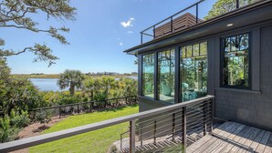 A modern house with a balcony overlooking a lake, surrounded by lush greenery. - Ocean, golf and lagoon views, complete renovation luxury home (Kiawah Island)