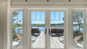 A view through a glass door to an outdoor deck with wooden flooring and two wooden chairs. - Ocean, golf and lagoon views, complete renovation luxury home (Kiawah Island)