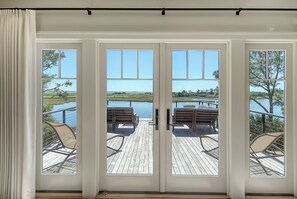 A view through a glass door to an outdoor deck with wooden flooring and two wooden chairs.
