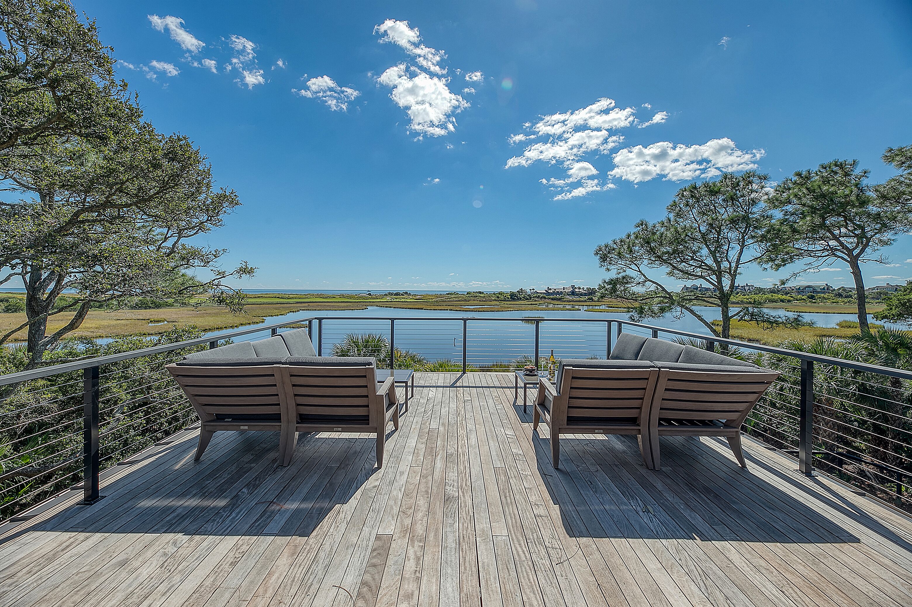 A wooden deck with two wooden chairs and a table, overlooking a body of water and a distant landscape.