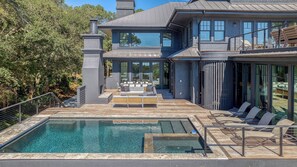 A modern house with a swimming pool, outdoor seating, and a large glass door.