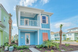 A two-story building with a balcony, a door, and a small garden area with plants. - Disney near Resort: 2BR Cottage w Private Pool (Kissimmee)