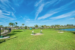 A park with a clear sky, a fenced area, and a body of water in the background.