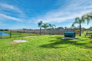 A fenced outdoor area with a grassy lawn, a water feature, and a green bench.