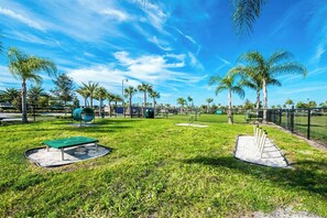 A park with a playground, a green bench, and palm trees.