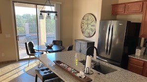 Een keuken met een granieten aanrecht, een roestvrijstalen koelkast, een eethoek met een tafel en stoelen, en een grote wandklok.