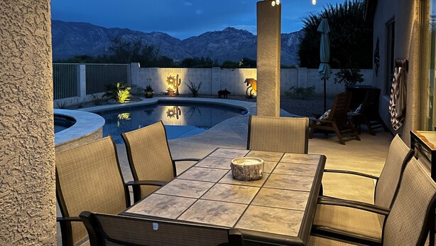 Een overdekt terras buiten met zwembad, zithoek en decoratieve verlichting.