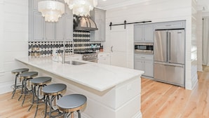 A modern kitchen with a central island, bar stools, stainless steel appliances, and decorative lighting. - Private Pool And Gulf Views- Sugar Magnolia By Royal Destinations (Santa Rosa Beach)