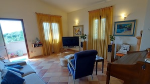 Una sala de estar con sofá, televisión, piano y mesa de comedor.