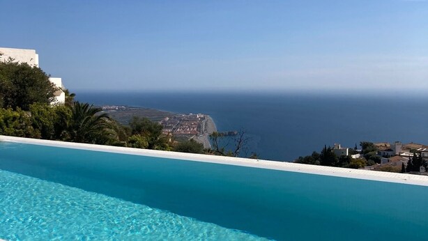 Une piscine d’un bleu éclatant, avec vue sur la mer et une ville côtière.