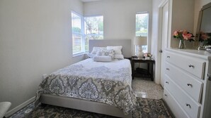 A bedroom with a bed, dresser, nightstand, and a window with blinds.