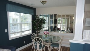 A dining area with a glass table, white chairs, and a large window with blinds. - Golf Resort Villa 509 within Walking Distance to Food and the Pool by RedAwning (Calabash)