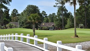 A wooden bridge with white railings leading to a golf course with a clubhouse in the background. - Golf Resort Villa 509 within Walking Distance to Food and the Pool by RedAwning (Calabash)