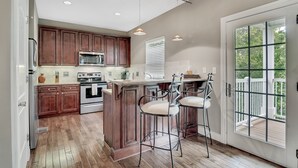 A kitchen with wooden cabinets, a central island with bar stools, a large window, and a view of a deck. - Birdie's Paradise 2 Bedroom Villa by RedAwning (Branson)